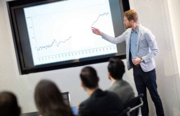 a man standing in front of a screen pointing at a graph